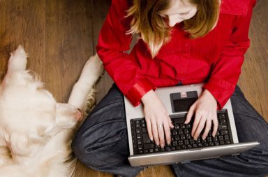 Woman sitting down with her laptop and dog sitting next to her.